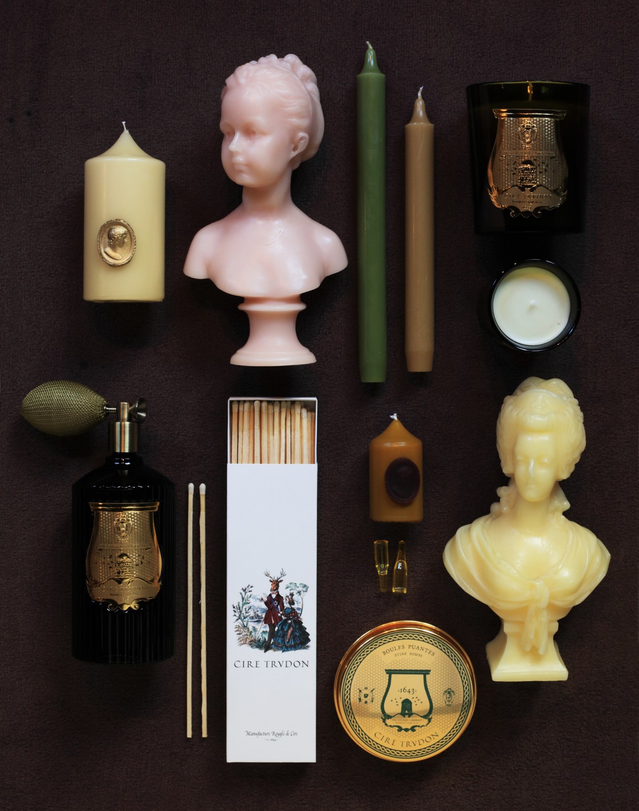 A selection of Cire Trudon candles, busts, and accessories arranged on a dark background.