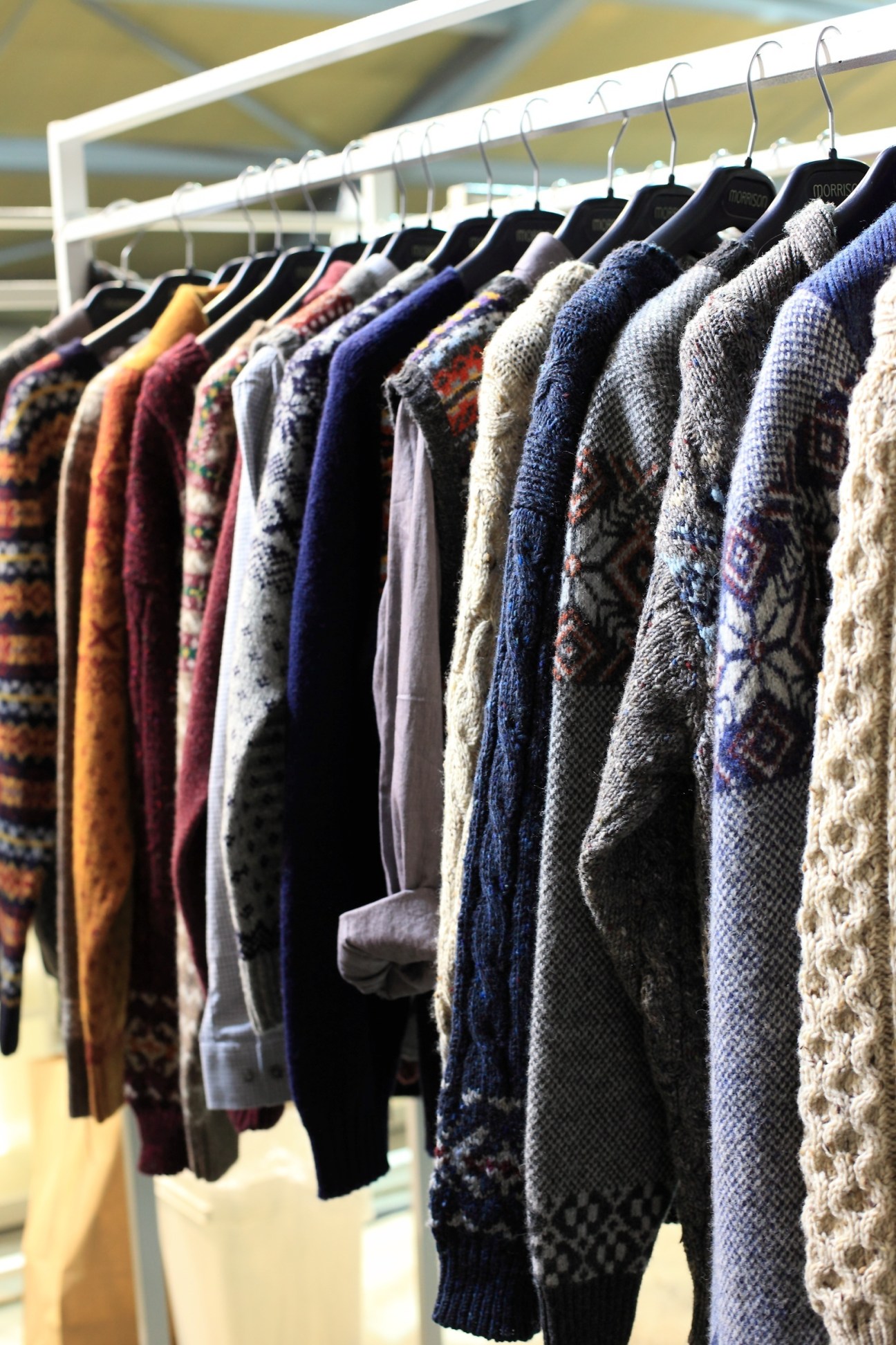 Morrison knitwear in various colors and Fair Isle patterns hanging on a metal rail.