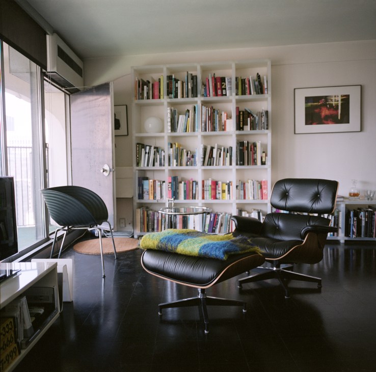 Modern living room with mid-century furniture, built-in white shelving, and curved balcony overlooking Chicago.