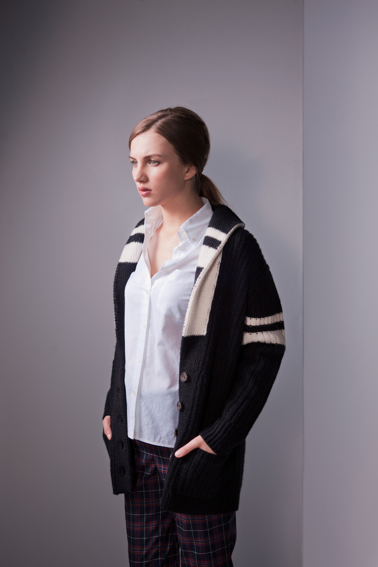 Woman wearing a black cardigan with cream stripes, white button-up shirt, and navy plaid trousers.