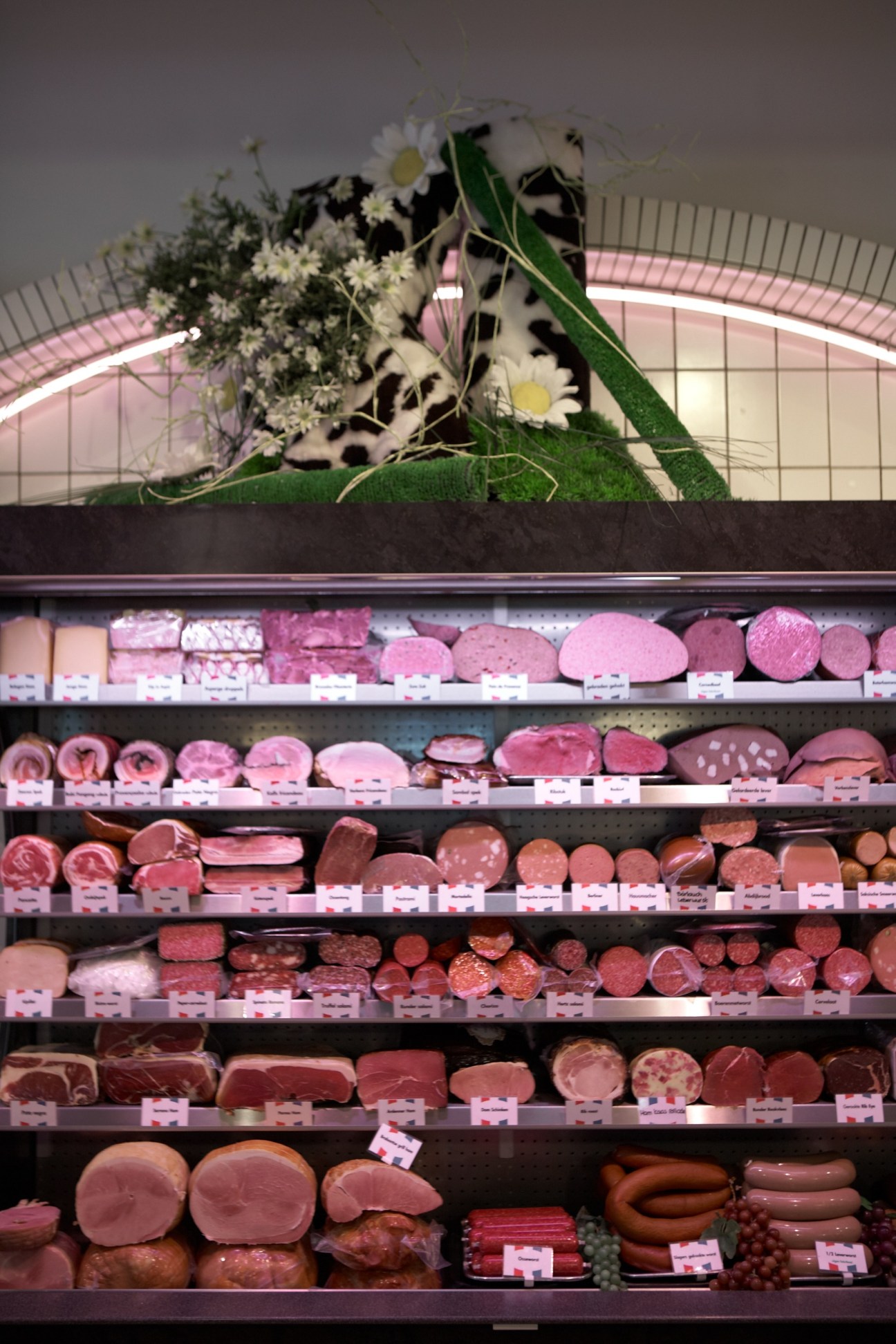 Shelves of various cured meats and sausages at Offers & Offers butcher shop with decorative flowers above.