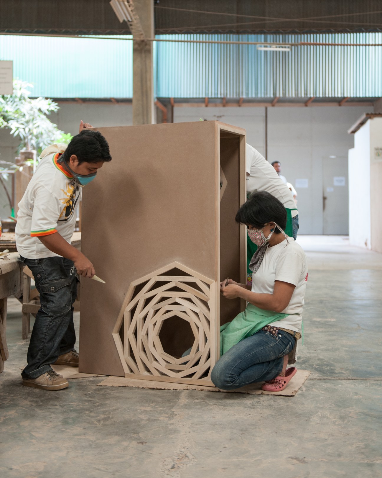 Two workers inspect a large wooden panel with a spiral cutout pattern at Stonesets factory.