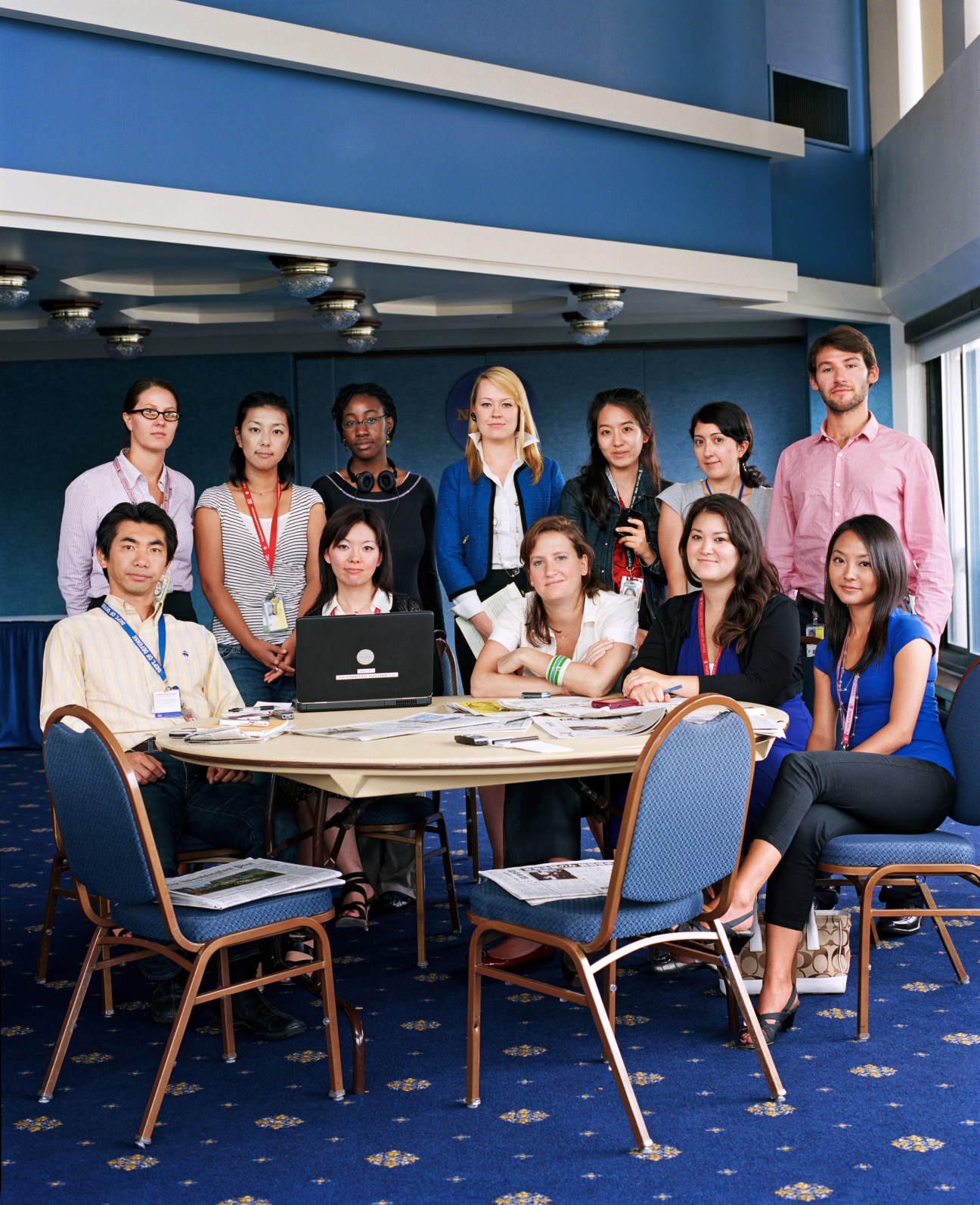 Japanese journalists from Nippon TV pose in a blue hotel conference room with laptops and materials.