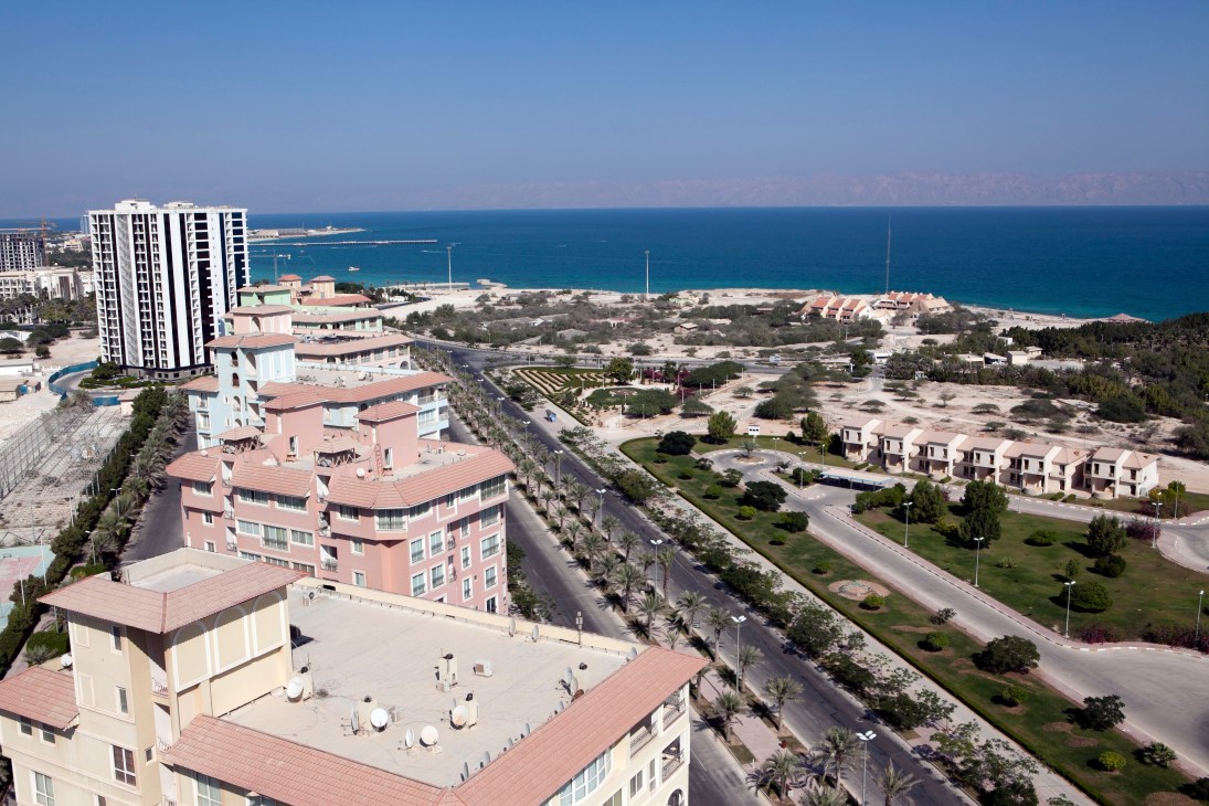 Aerial view of Kish island's coastal development with modern apartment buildings, Persian Gulf waters, and sparse desert vegetation.
