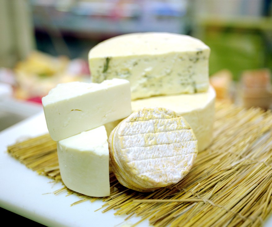Selection of Finnish cheeses displayed on straw, including creamy blue cheese and goat milk cheddar varieties.