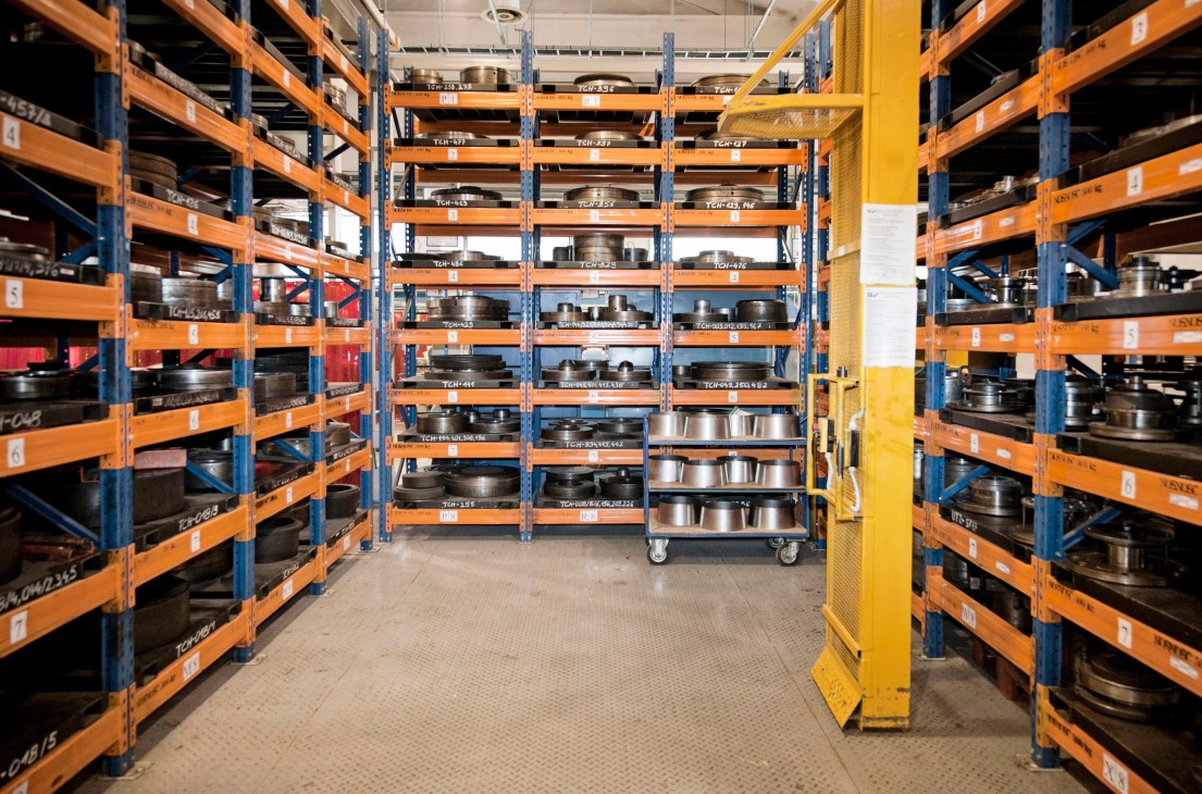 Industrial warehouse with orange and blue shelving units storing metal aircraft components and parts.
