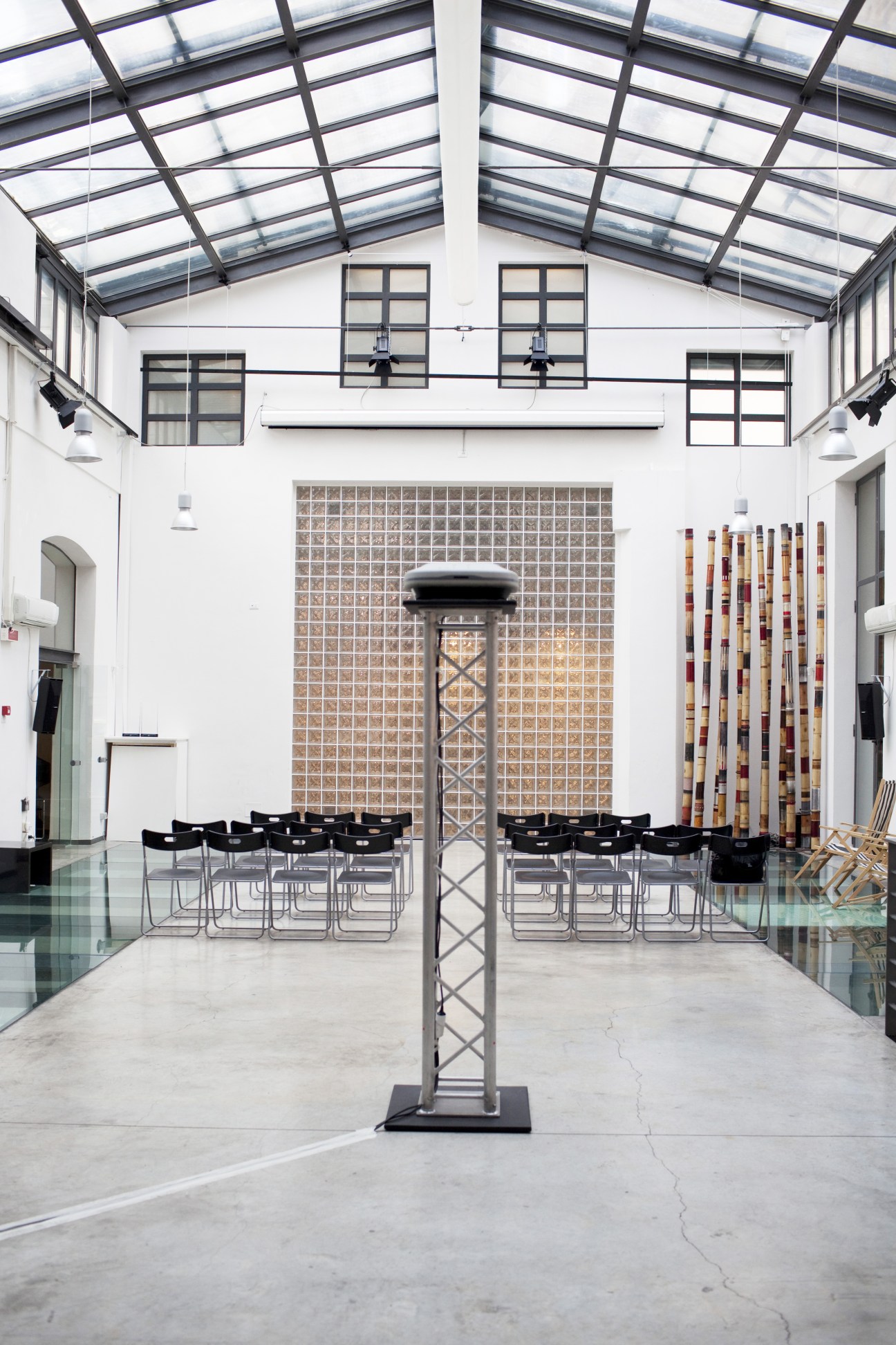 Modern gallery space with skylights, industrial column, tiered seating, and colorful material installation.