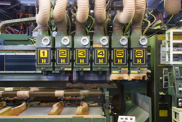 Industrial factory machine with multiple curved dust collection hoods and yellow numbered controls for woodworking at Maruni.