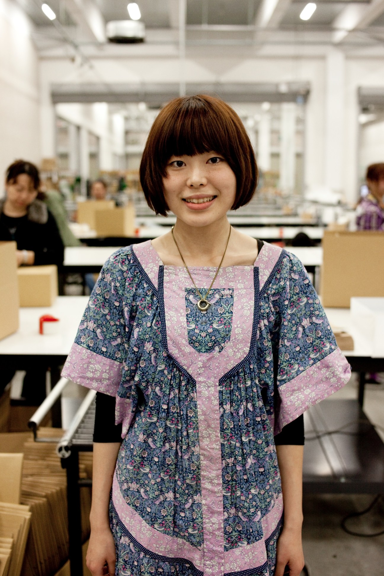 Sayaka Kimura, 24, smiles at the camera in Start Today's open-plan office with colleagues working in the background.