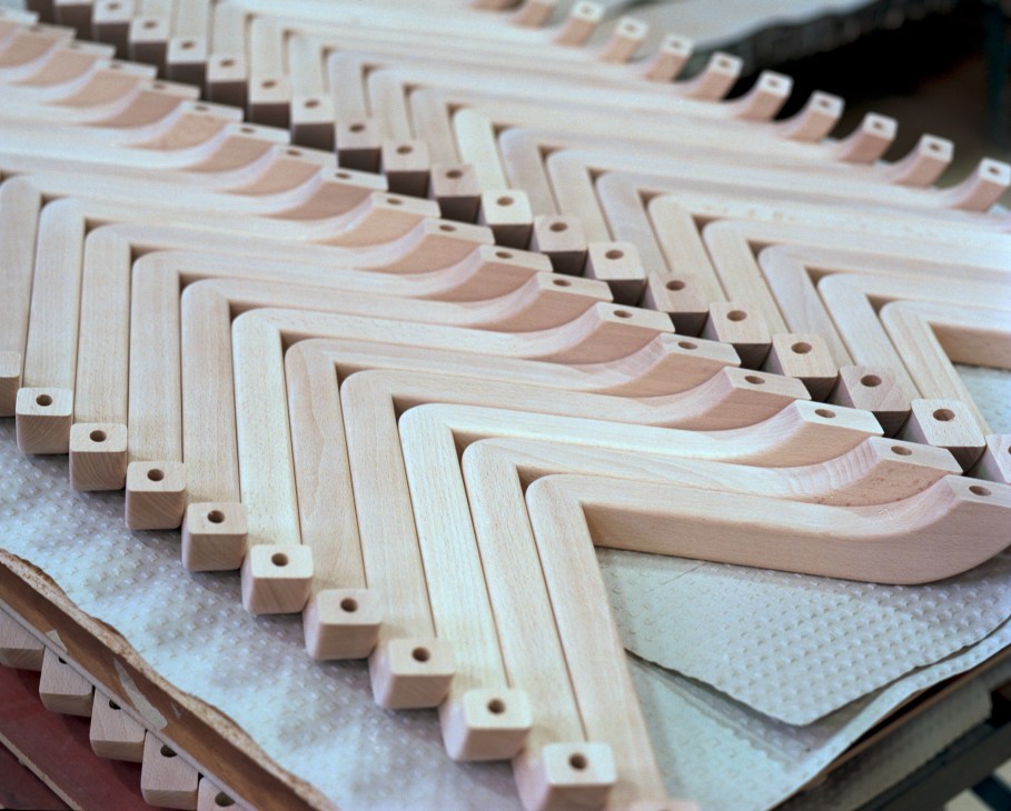 Rows of unpainted wooden chair armrests with drilled holes, arranged in organized stacks.