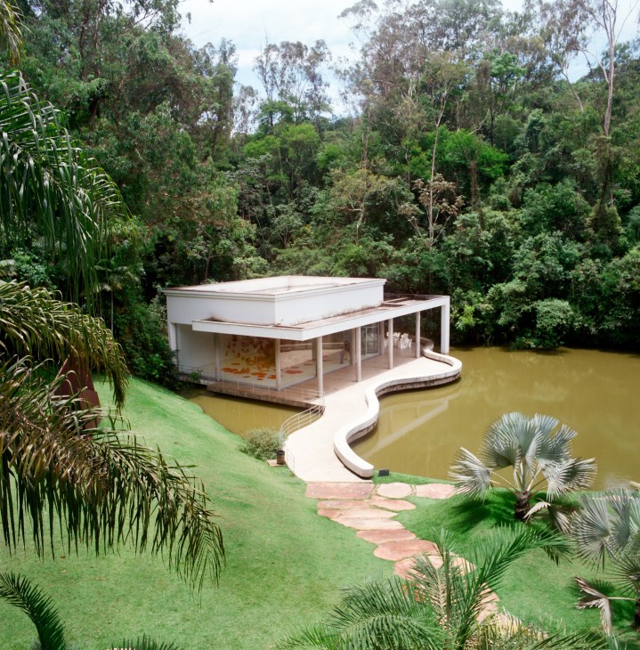 Modern white building with curved architecture overlooking a river surrounded by lush green forest at Inhotim art centre.