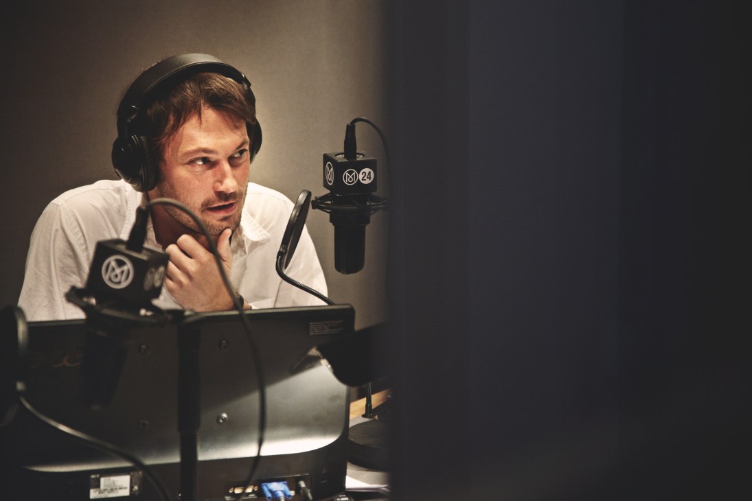 Robert Bound recording at a microphone wearing headphones in a radio studio