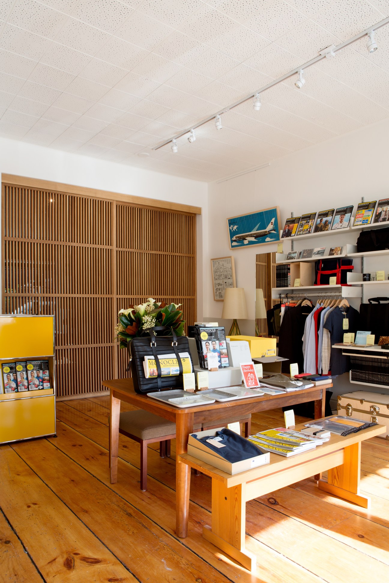 Interior of Monocle Shop in Toronto featuring wooden sliding screens, display tables, shelving with magazines and products, and clothing racks.