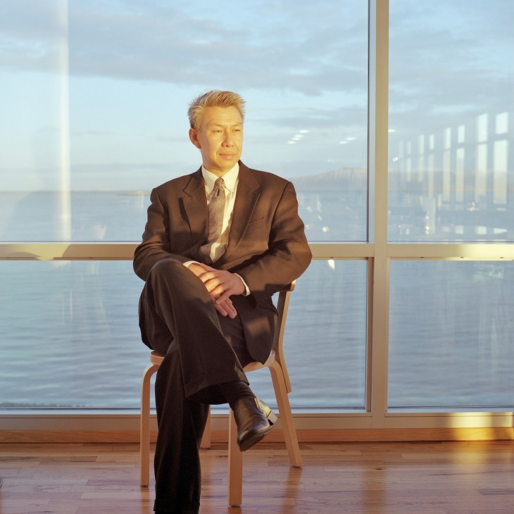 Carbon Recycling International CEO KC Tran sits on a wooden chair by a large window overlooking water.
