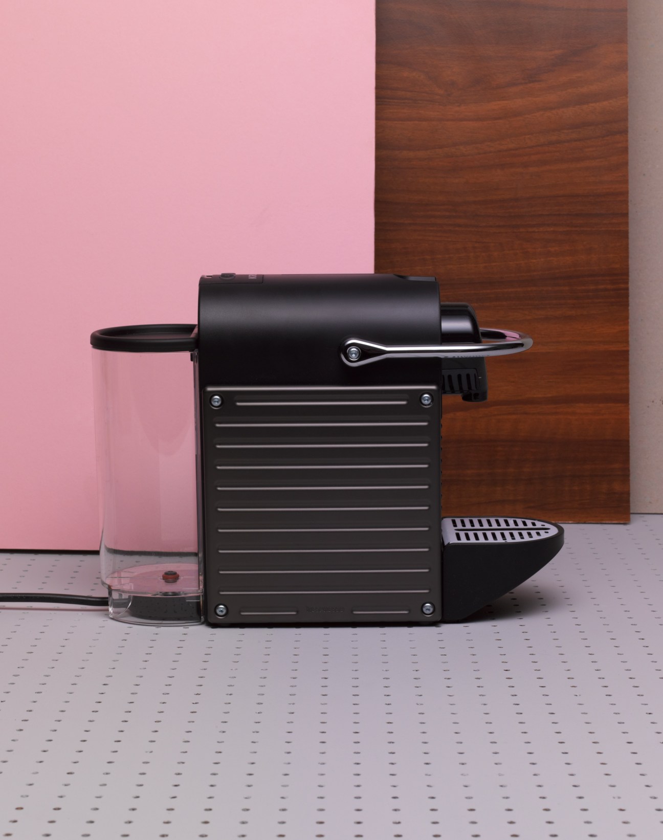 Nespresso Pixie coffee machine in black with a glass cup on a pink background.