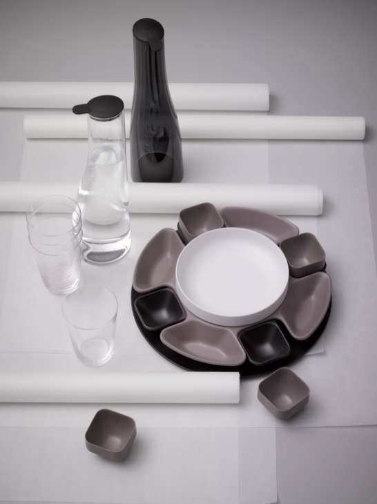 Italesse tableware collection featuring a white plate with gray and black compartments, glasses, and a black carafe on white paper.