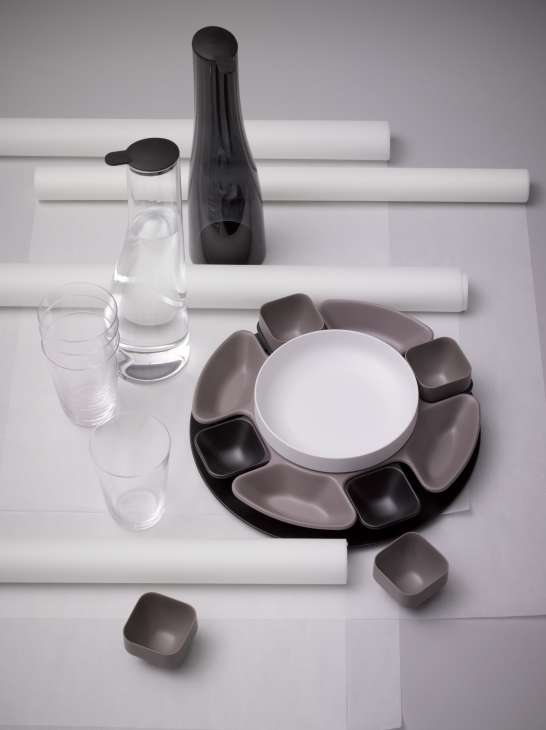 Italesse tableware collection featuring a white plate with gray and black compartments, glasses, and a black carafe on white paper.