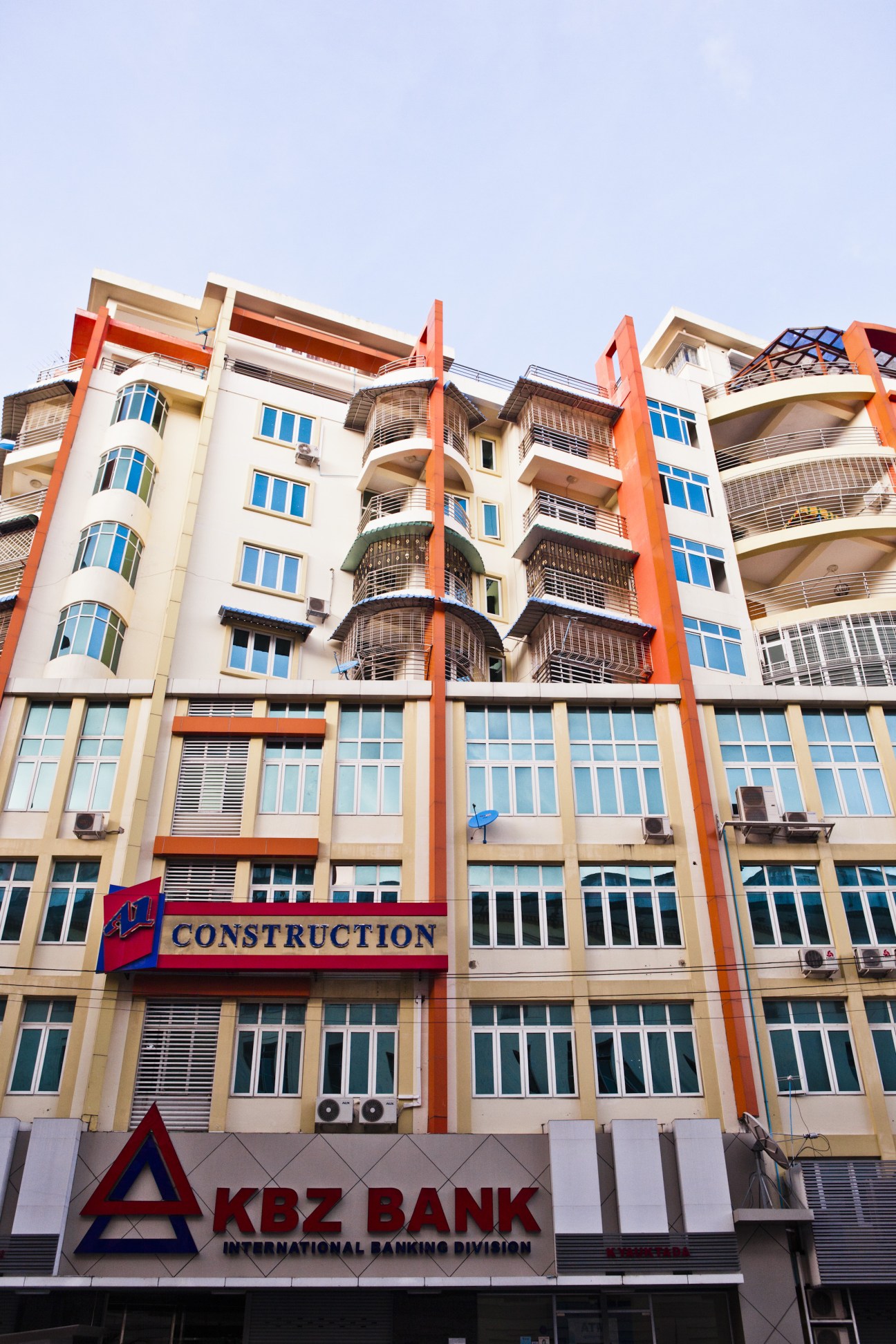 Modern multi-story building with cream and orange facade, blue windows, and KBZ Bank storefront on ground level in Rangoon.