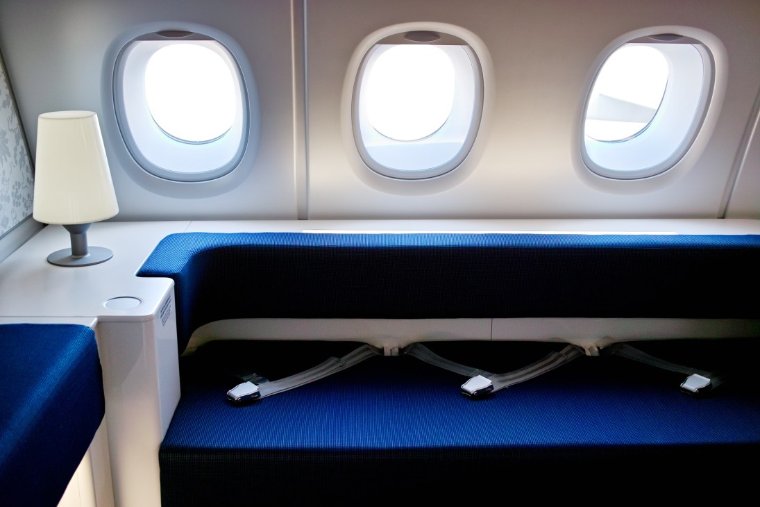Korean Air A380 first class cabin with blue seating, white side table with lamp, and three illuminated cabin windows.
