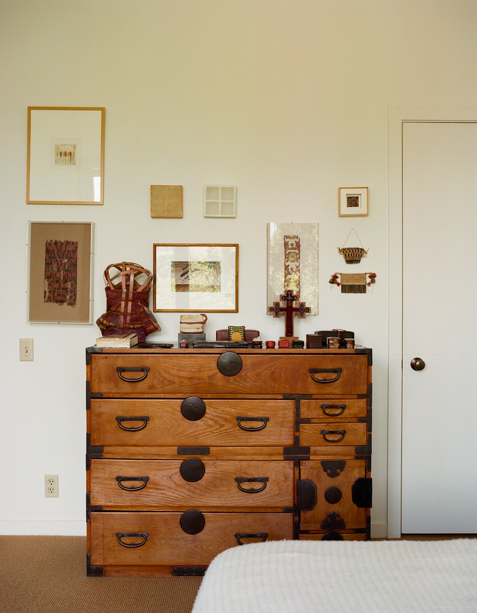 A wooden Japanese tansu chest with metal hardware displaying art objects and textiles above it in a bedroom.