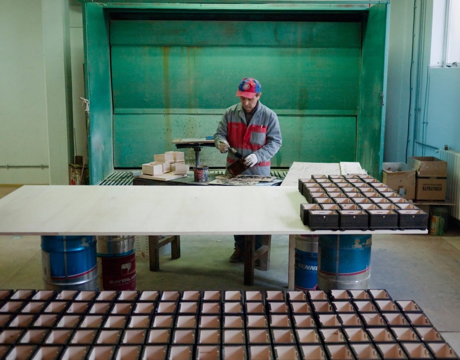 Craftsman in red cap and work clothes carving wooden money boxes at Rukotvorine workshop.