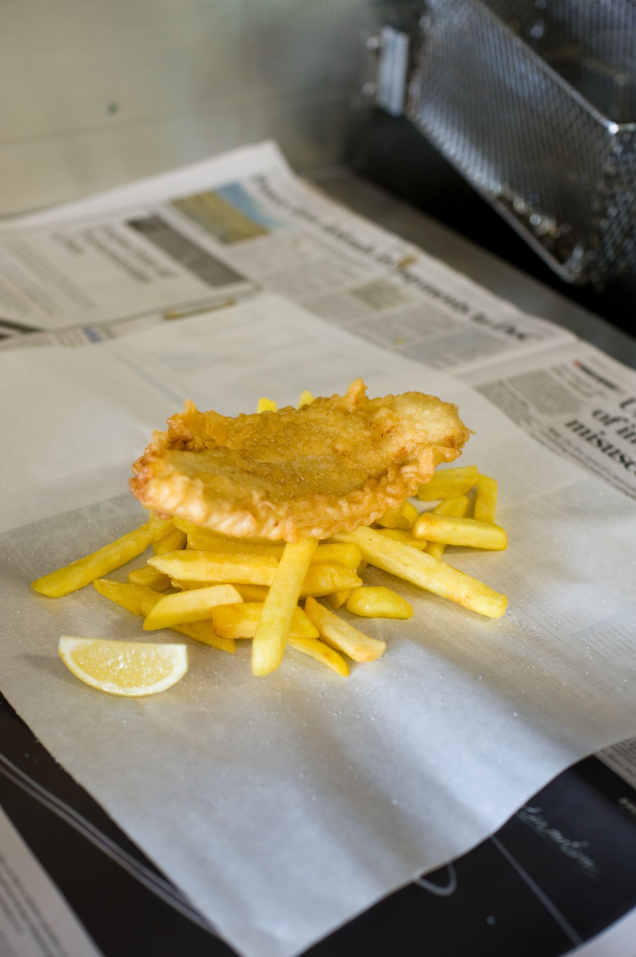 Battered fish and chips served on paper with a lemon wedge.