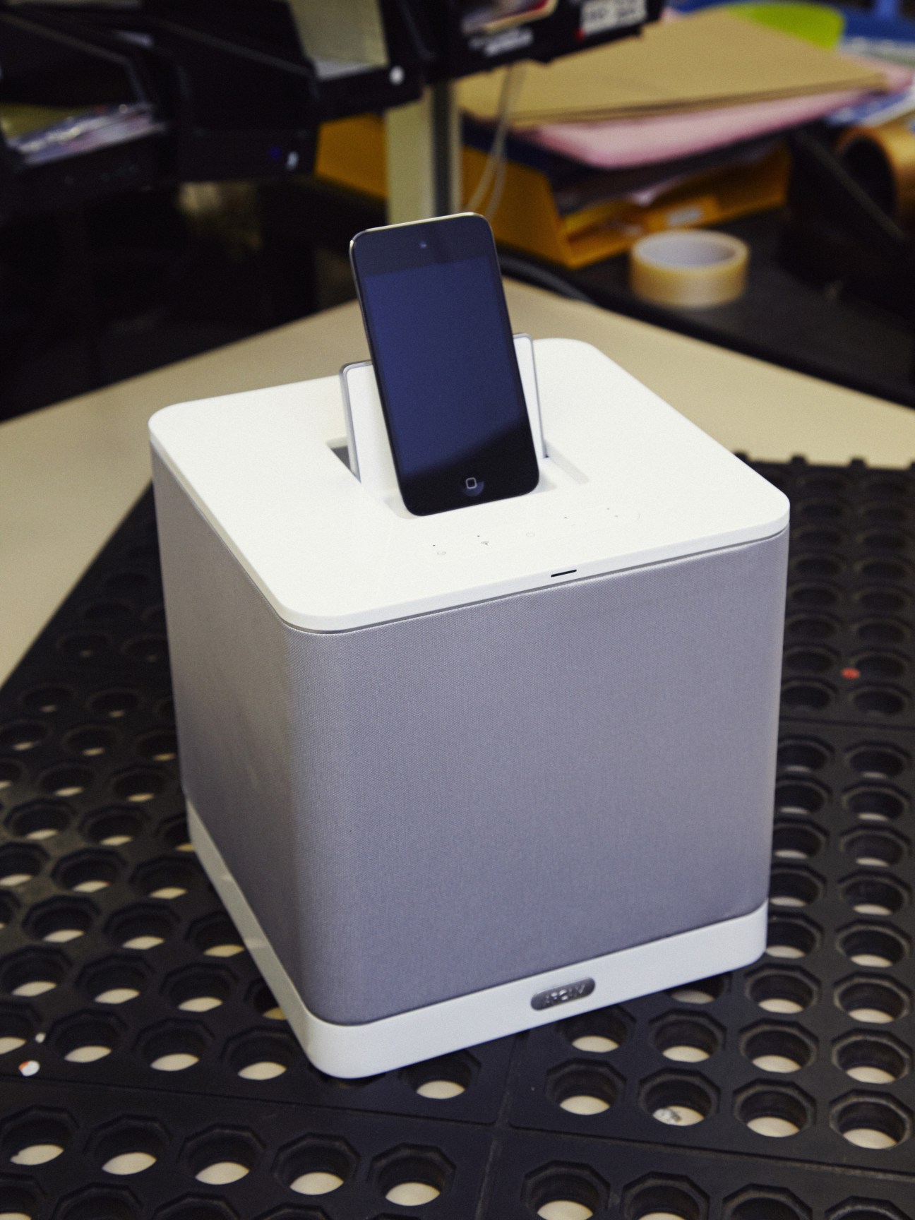 Arcam's R-Cube white speaker dock with smartphone inserted into top slot on perforated table