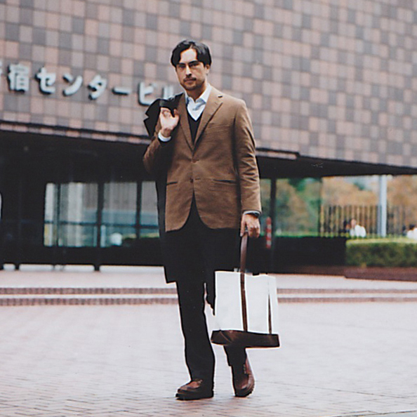 Man in business attire holding a leather document case outside a modern brick building.