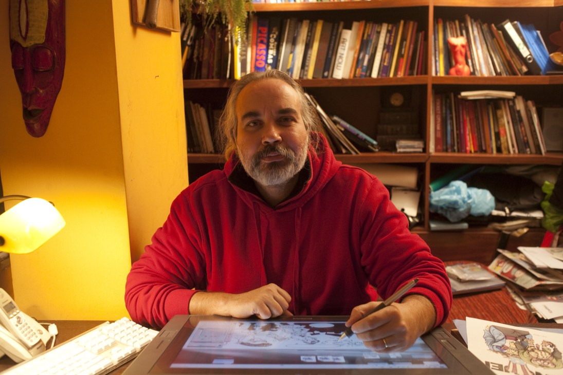Bahadir Baruter, cartoonist at Penguen satirical weekly magazine, sits at desk working on digital tablet in colorful office.