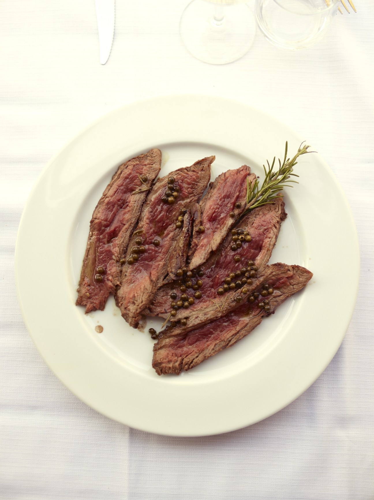 Grilled Chianina sirloin sliced and plated with green peppercorns and rosemary garnish.