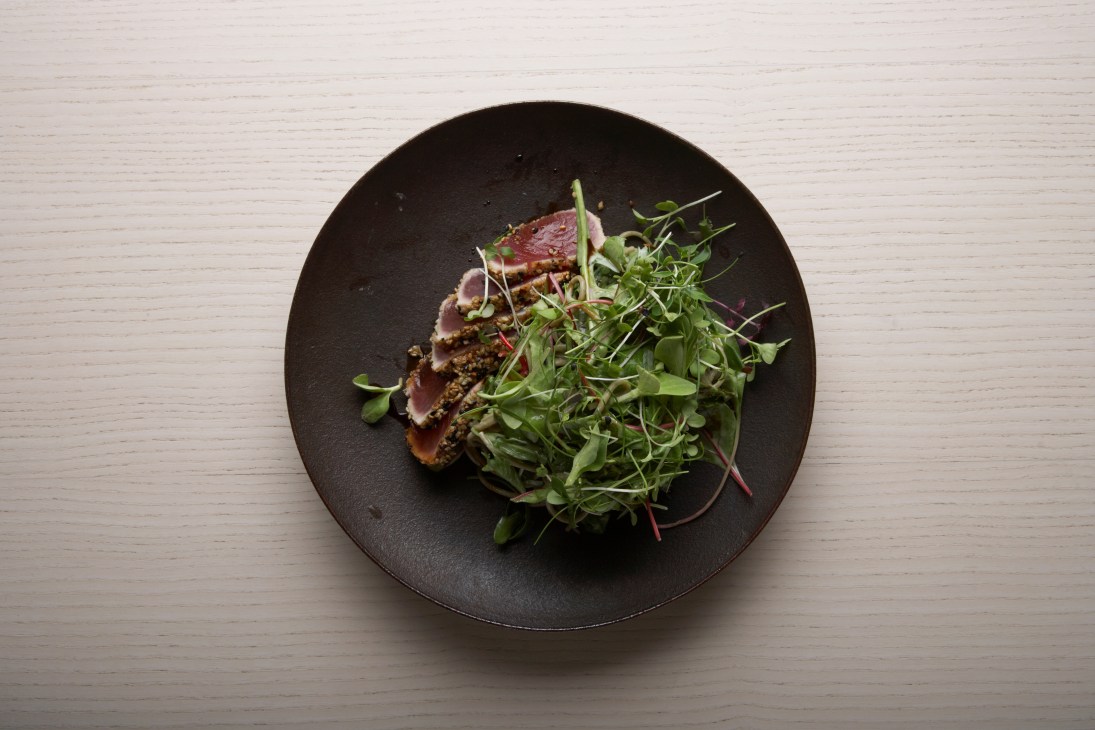 Seared tuna and green tea soba salad with wasabi jelly and tonburi on a black plate.