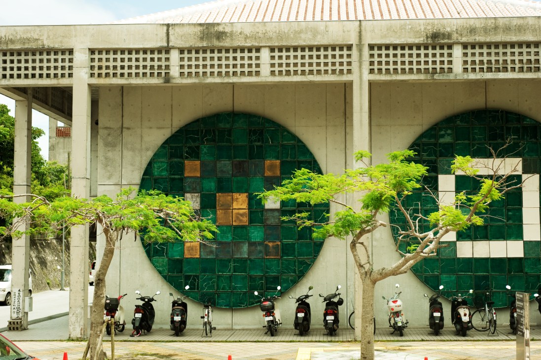 Library building of Okinawa Prefectural University of the Arts with large circular green tile window and parked scooters.