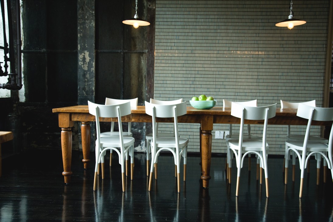 André Balazs Properties kitchen with wooden table, white chairs, and warm pendant lighting in New York office.
