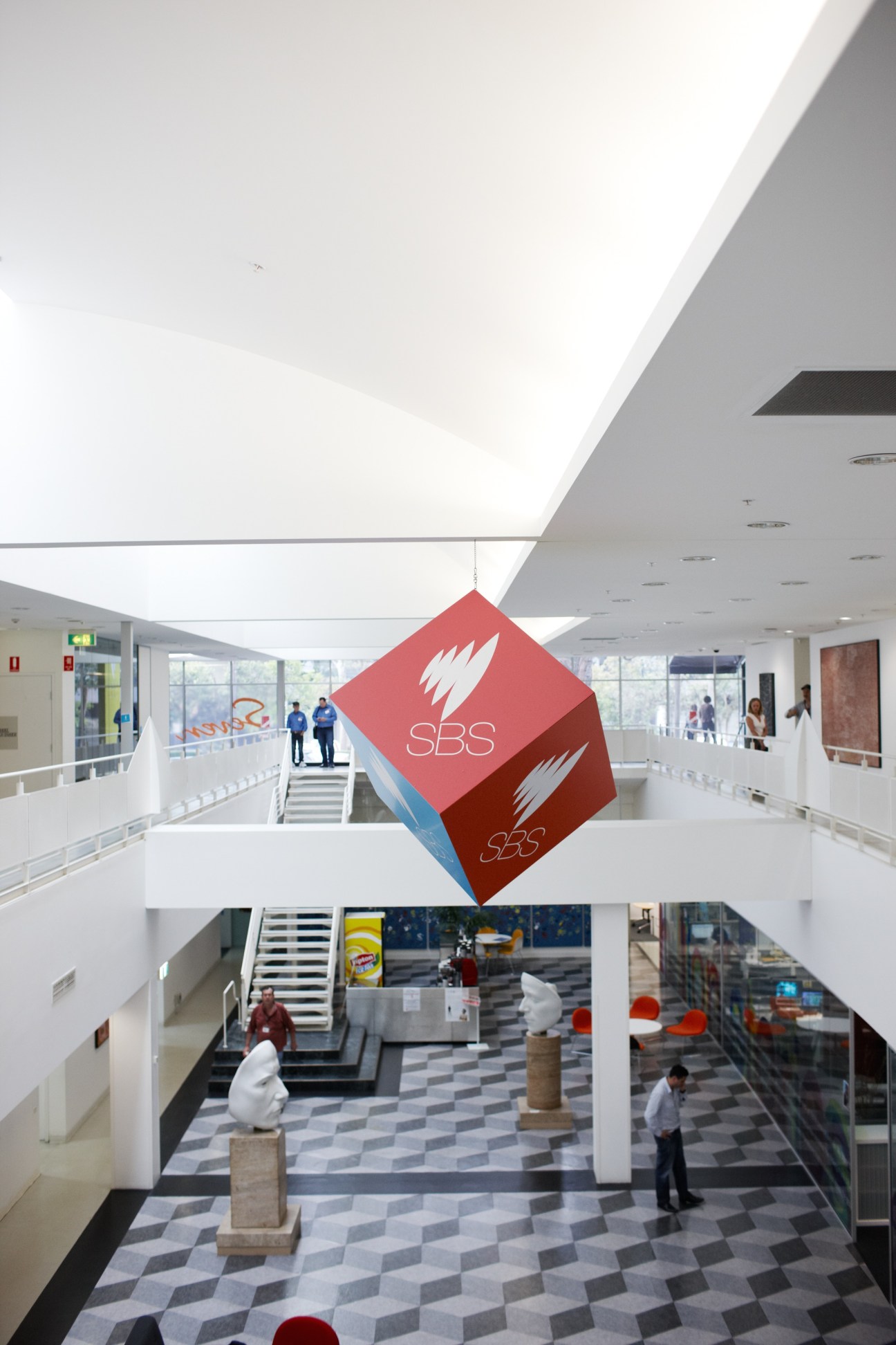 Modern atrium at SBS headquarters with red diamond-shaped logo suspended from ceiling.