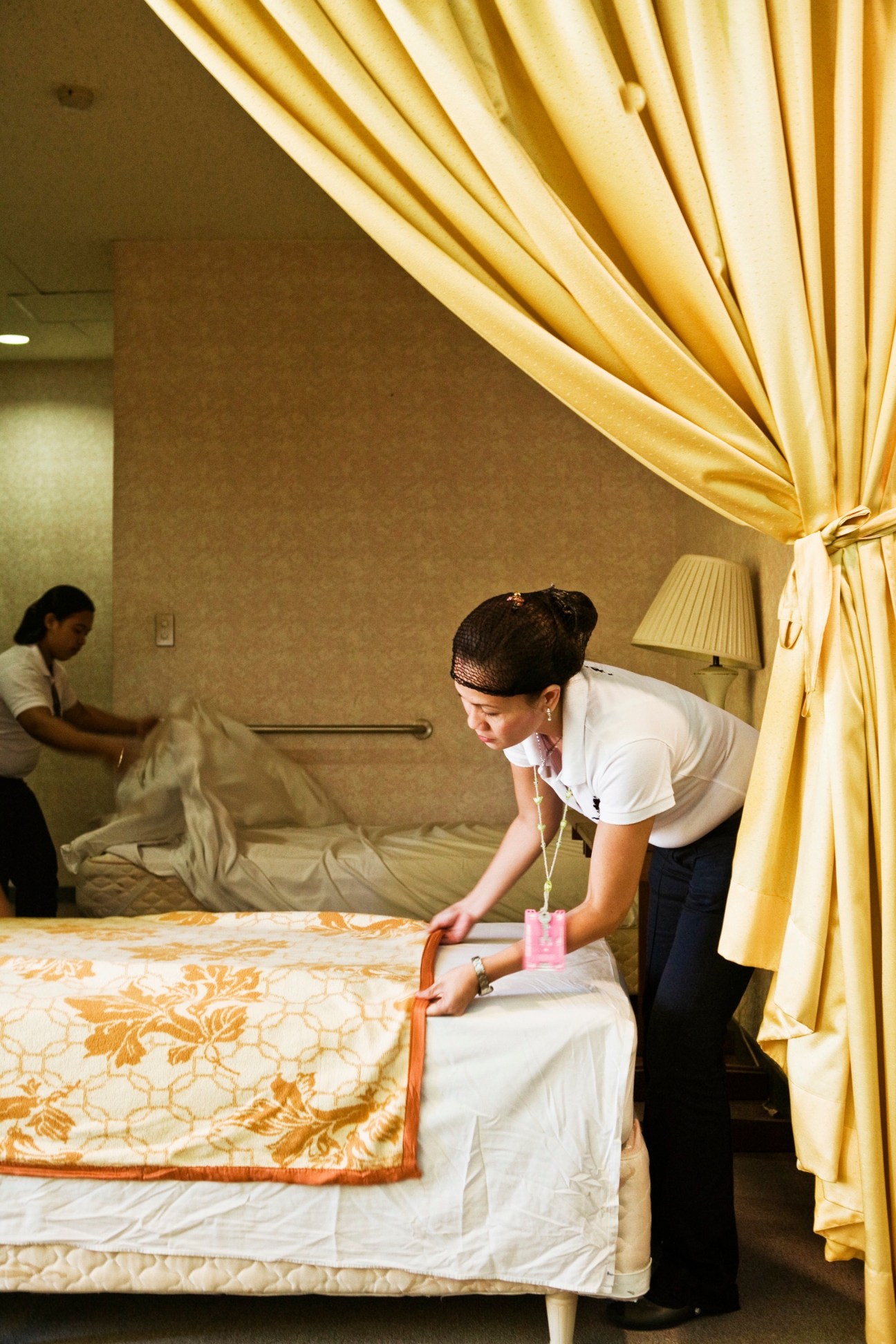 Housekeeping student demonstrates bed-making technique in a mock hotel room during training.
