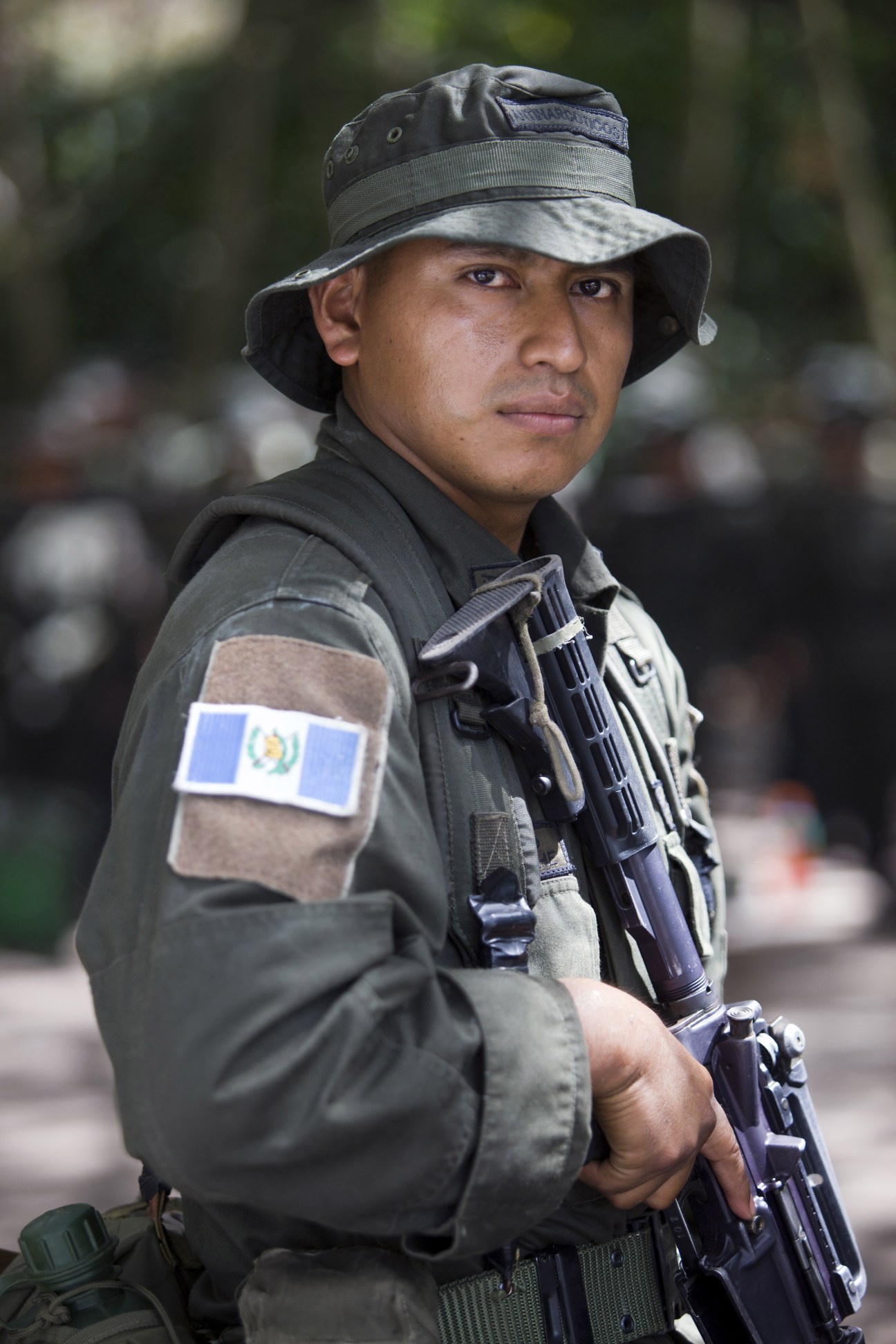 Guatemalan police student in uniform with rifle wearing a tactical hat and arm patch.