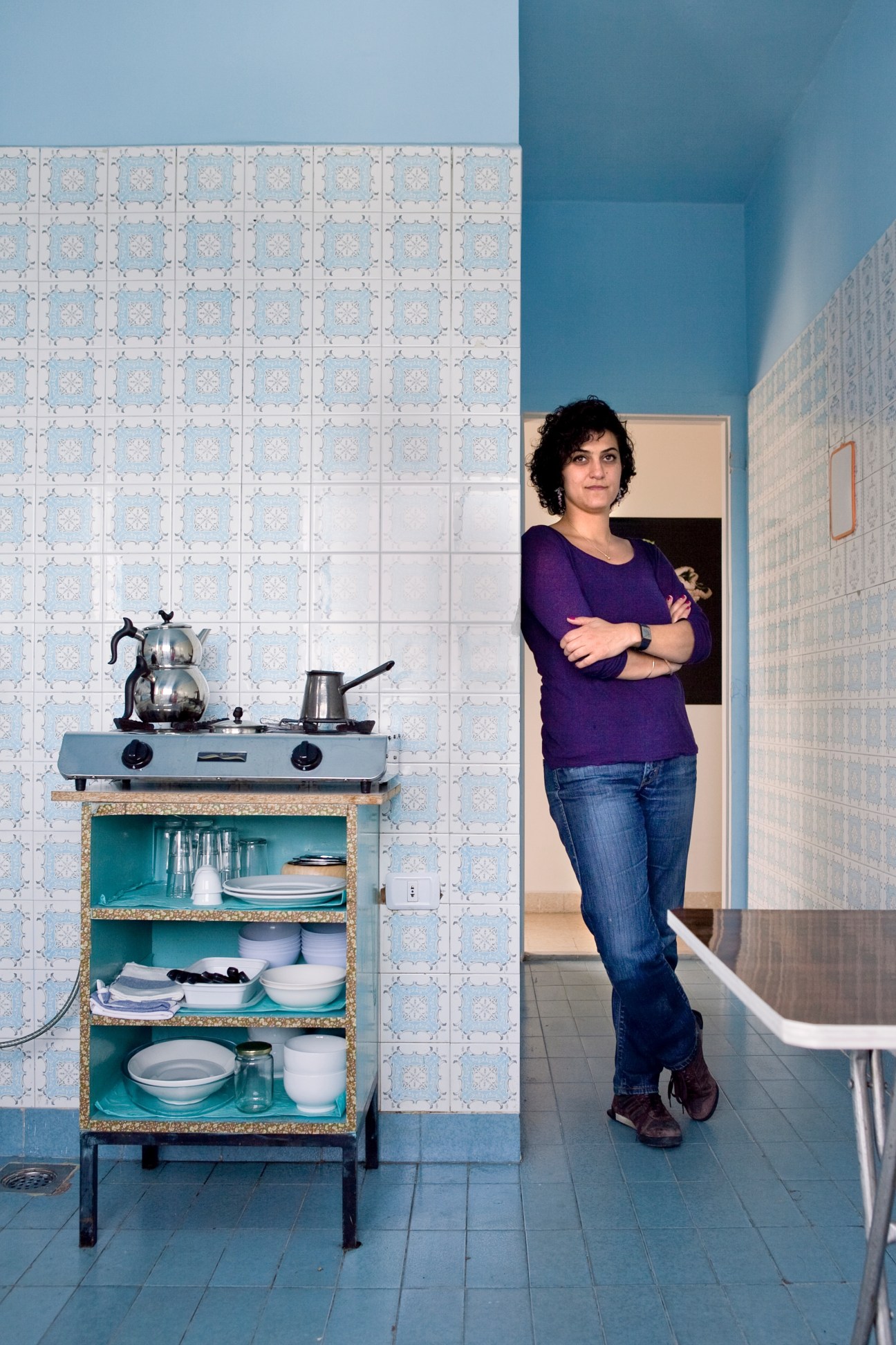 Artist Setareh Shahbazi standing in a kitchen with blue and white patterned tiles and turquoise shelving.