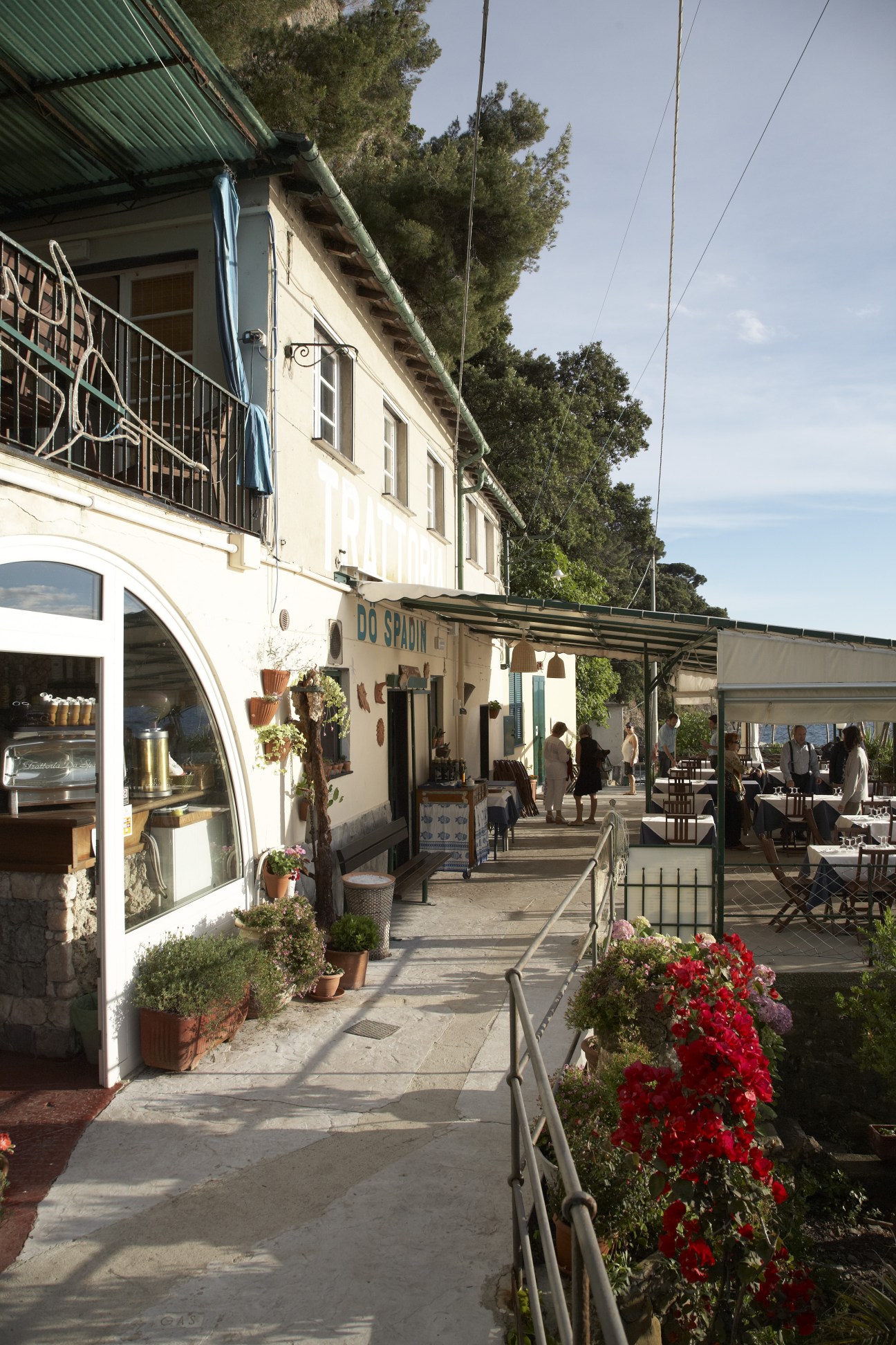 Outdoor waterfront dining area at Trattoria da Spadin with flowers and Mediterranean architecture.