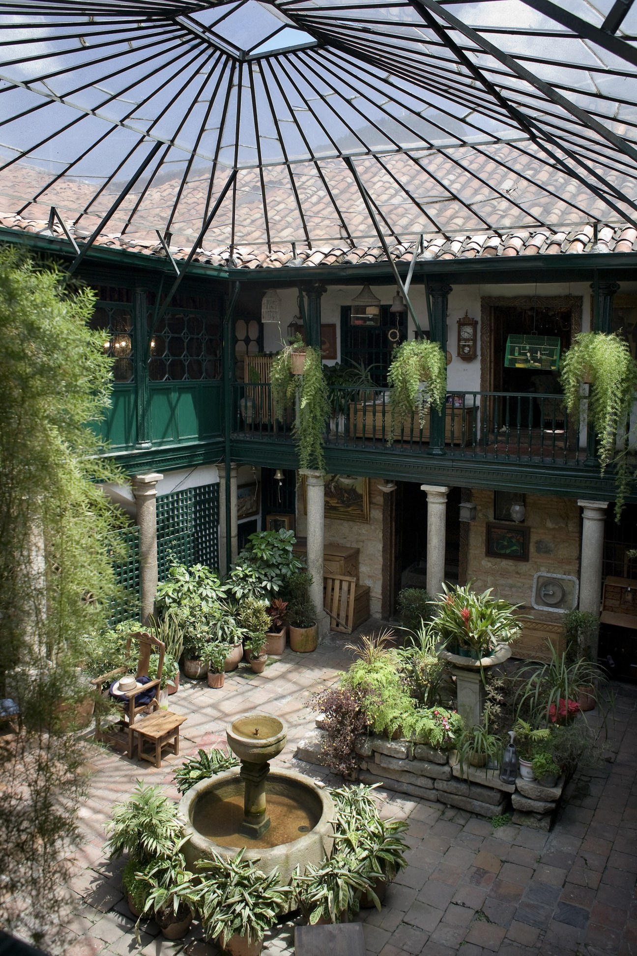 Courtyard of a colonial building with a fountain, potted plants, and a green-framed glass roof at Jaime Botero antique shop.