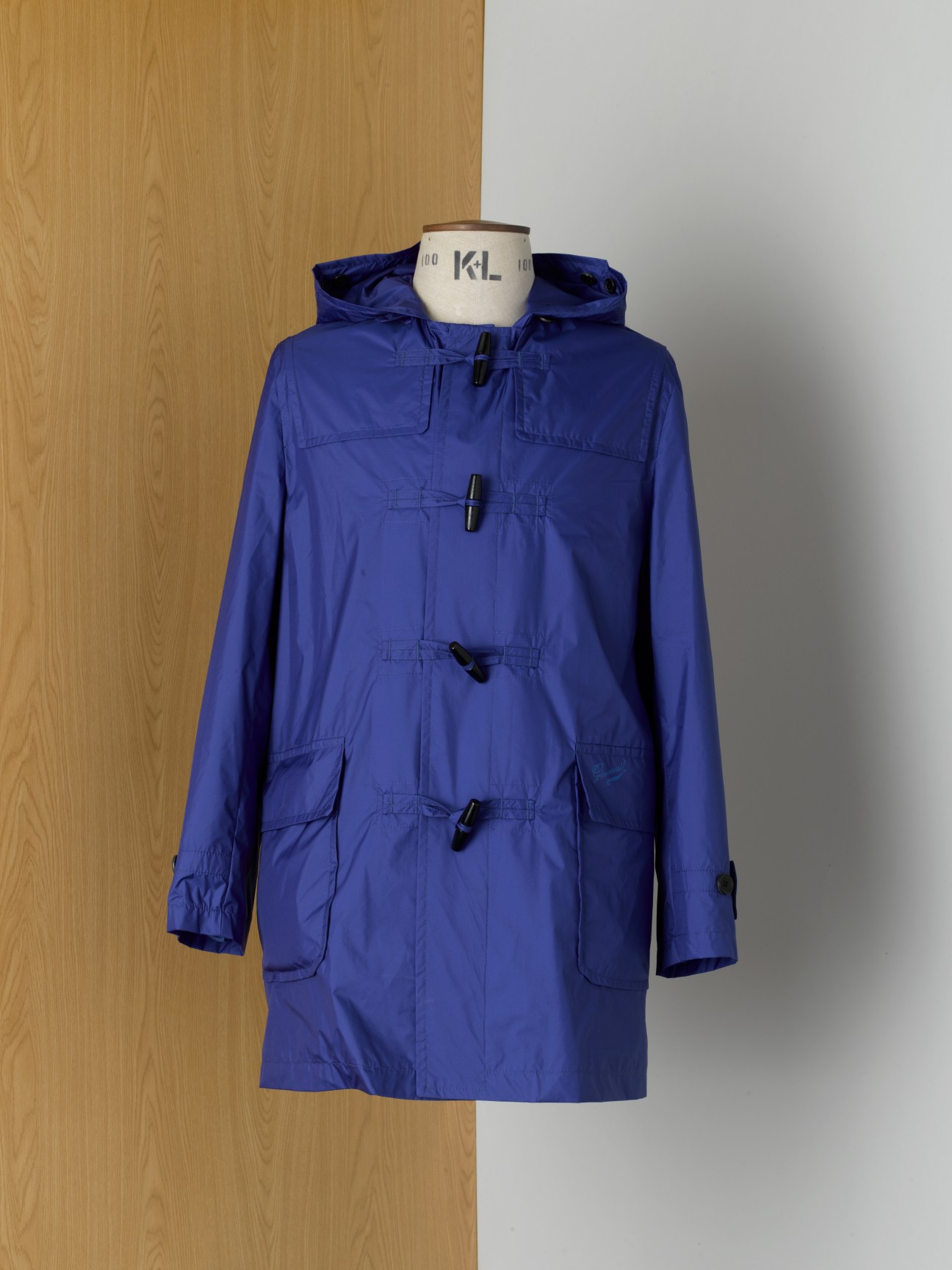 Blue Gloverall raincoat with toggle buttons and plaid lining displayed on a mannequin.