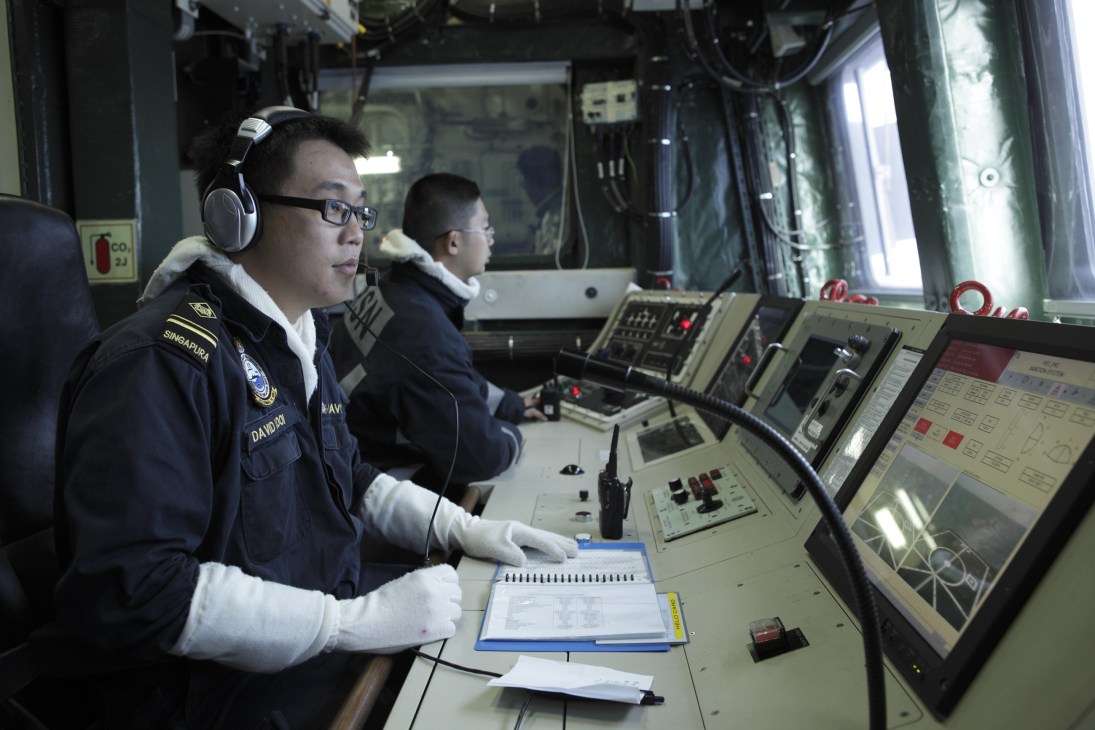 Singapore Navy servicemen coordinate test drills on the bridge of a warship, monitoring navigation and radar systems.