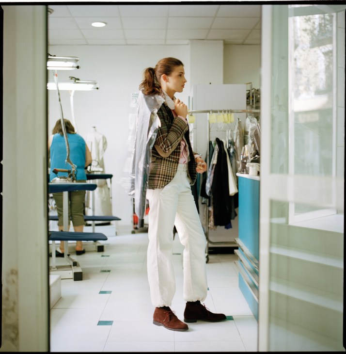 Woman in a dressing room wearing a plaid jacket, waistcoat, white trousers and brown shoes.