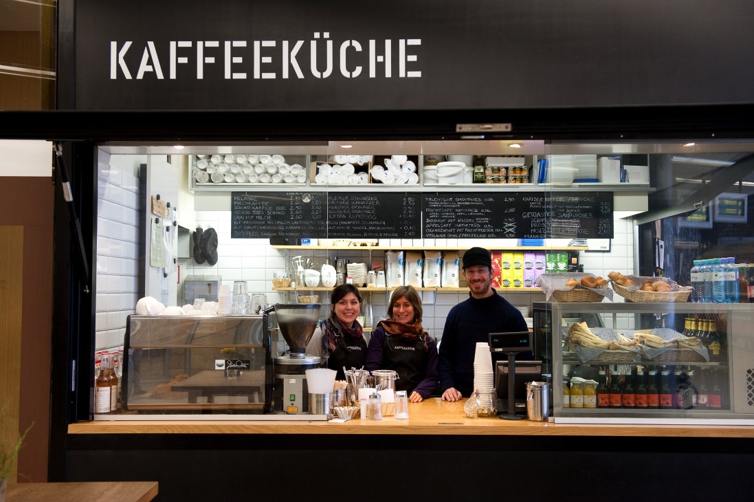 Kaffeeküche coffee stand in Vienna with three staff members behind counter with signage and menu board above