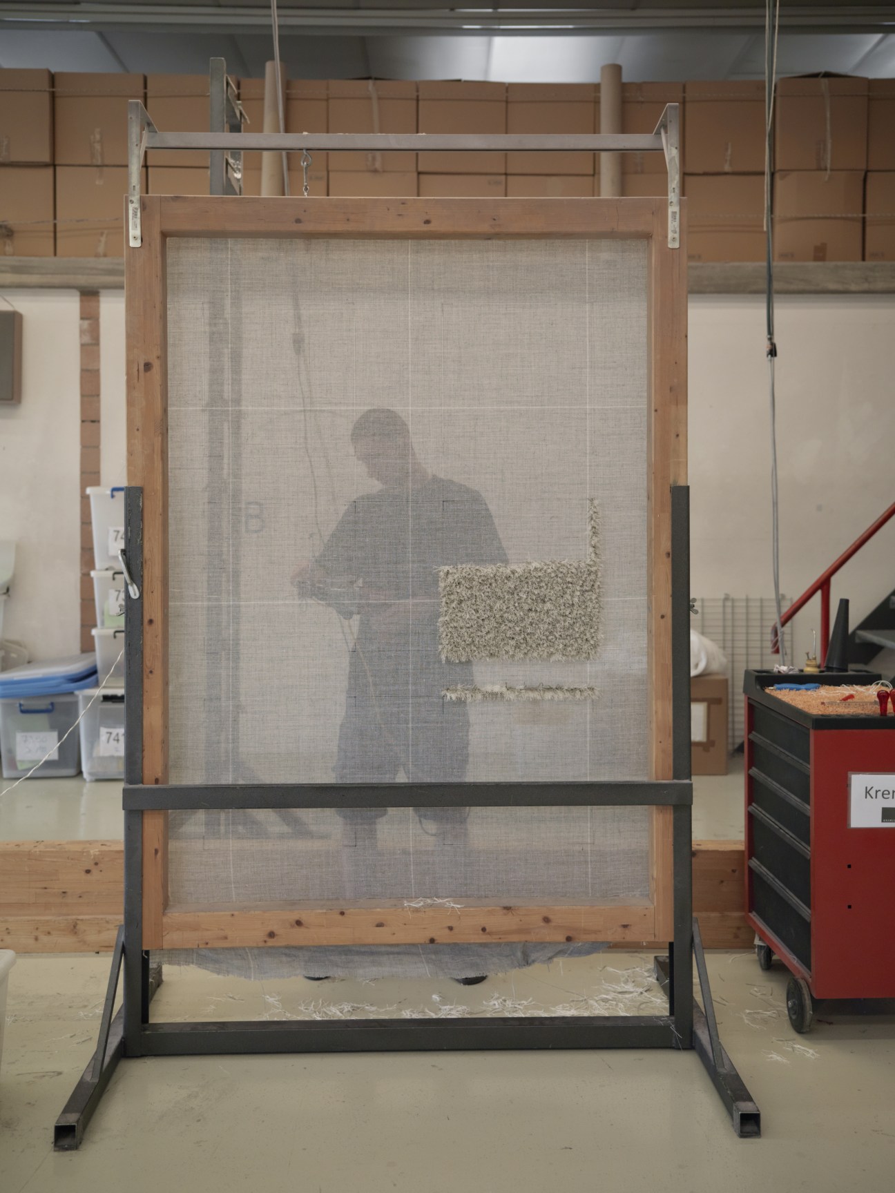 A worker mounts linen base material onto a large wooden frame in the Kramis carpet workshop.