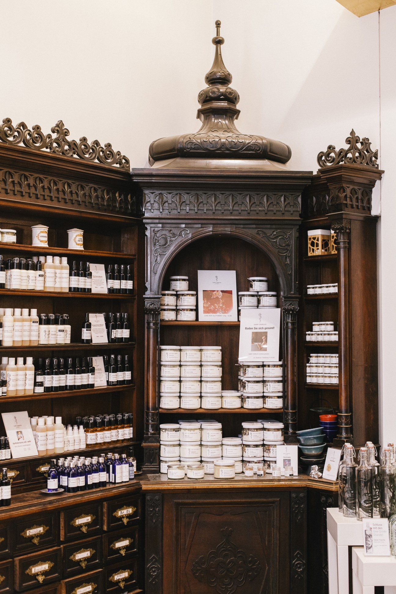 Ornate wooden apothecary cabinet with cream-colored jars and dark bottles displayed on shelves at Saint Charles Apotheke.