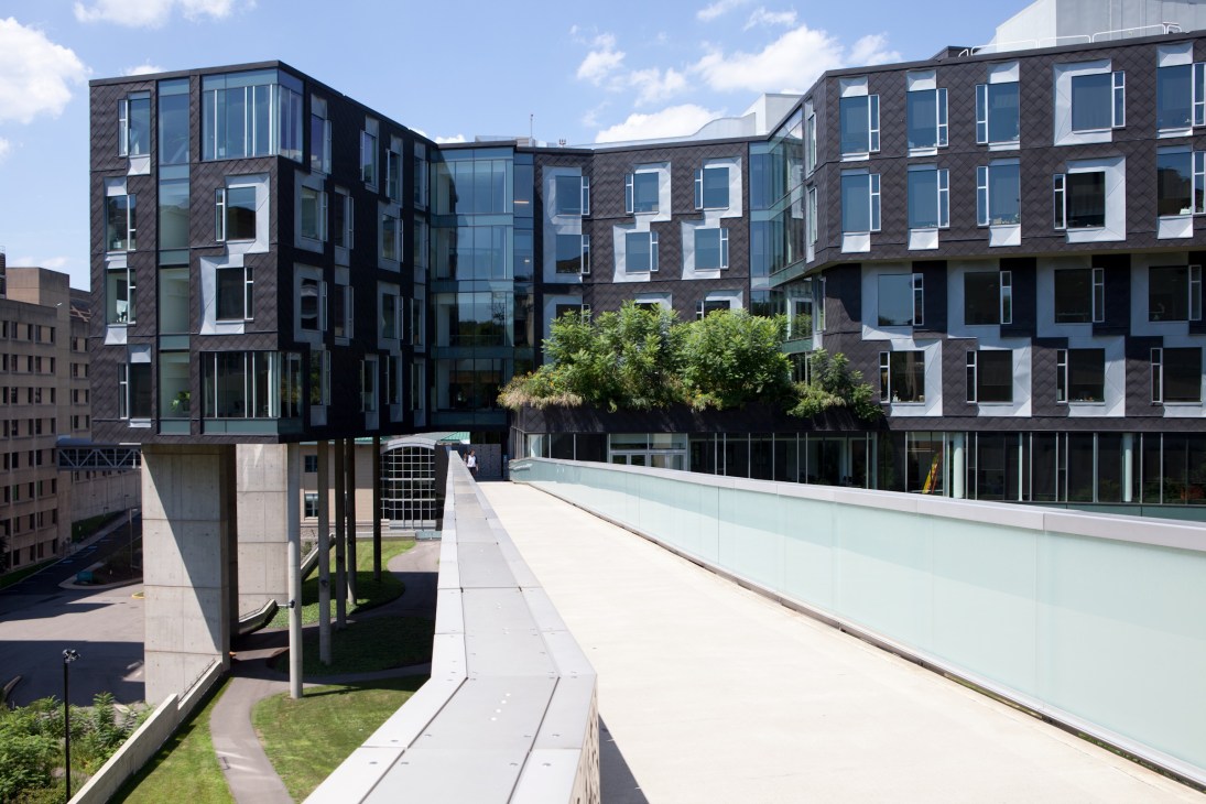 Modern dark brick and glass building complex with rooftop terrace featuring plants and greenery.