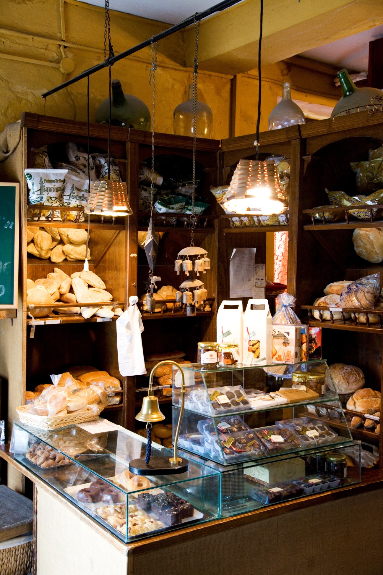Interior of Antigua Abacería's deli with wooden shelving, glass display cases of baked goods, and hanging pendant lights.