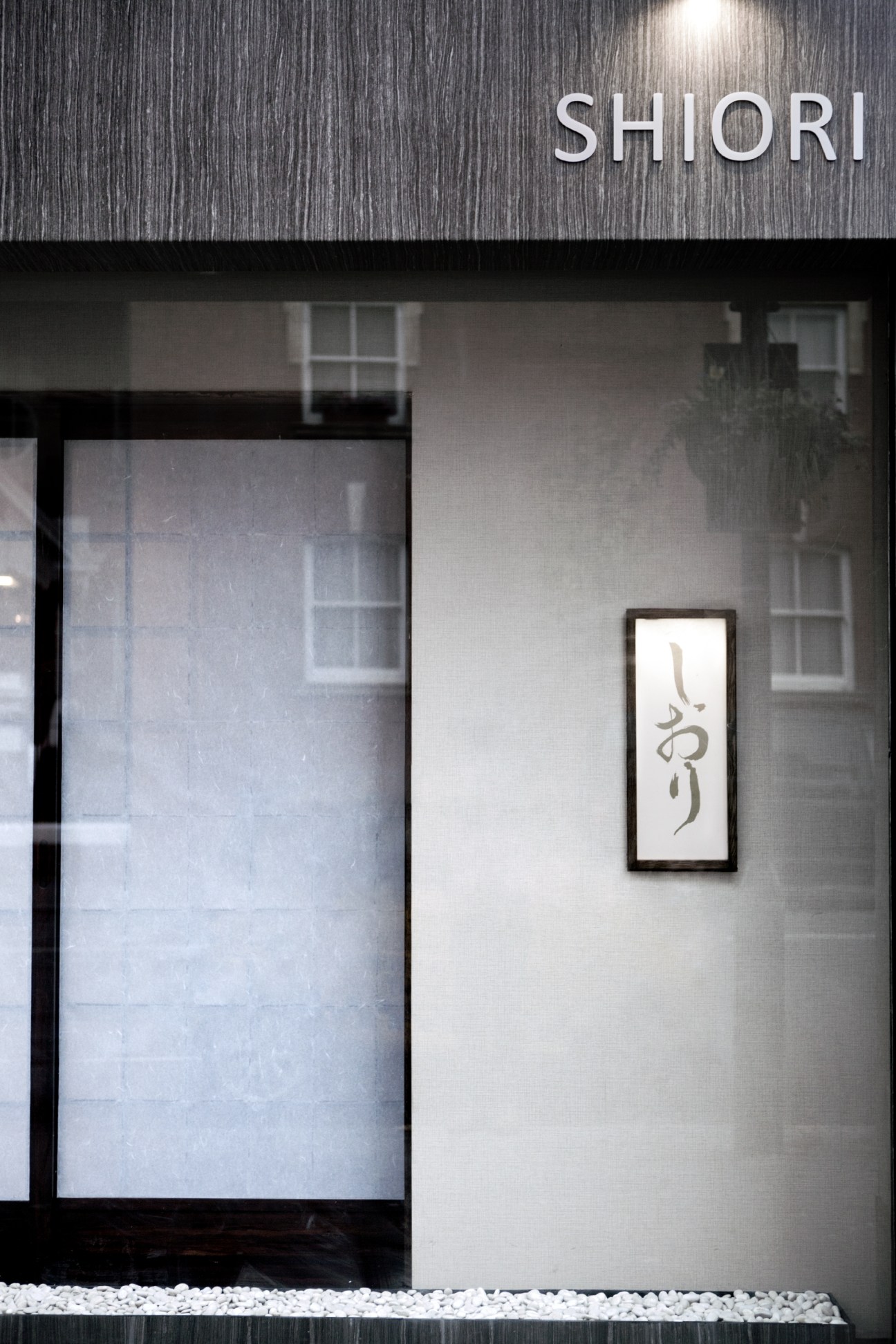 Shiori restaurant exterior in London with illuminated white signage and Japanese calligraphy artwork on the wall.