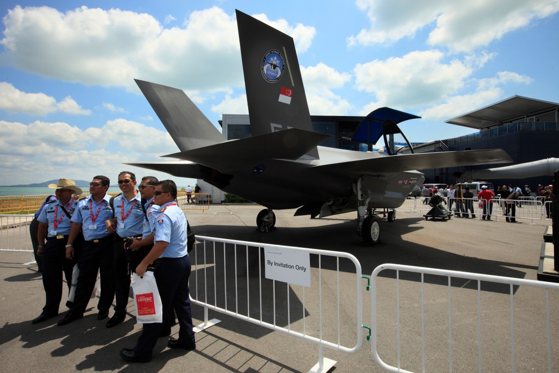 Military personnel stand before Lockheed Martin's F-35 fighter jet on display at an air show.