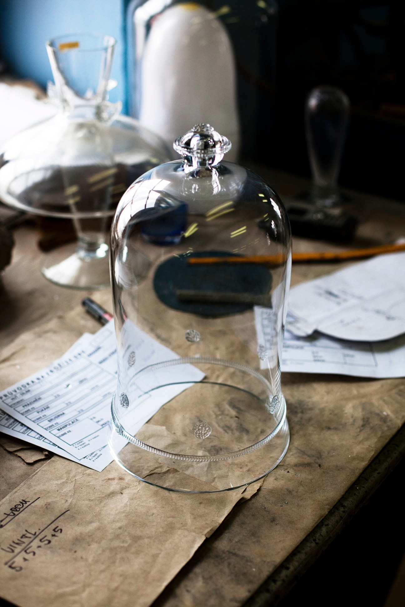 A handblown glass dome with finial sits on kraft paper among design sketches and other glass pieces.